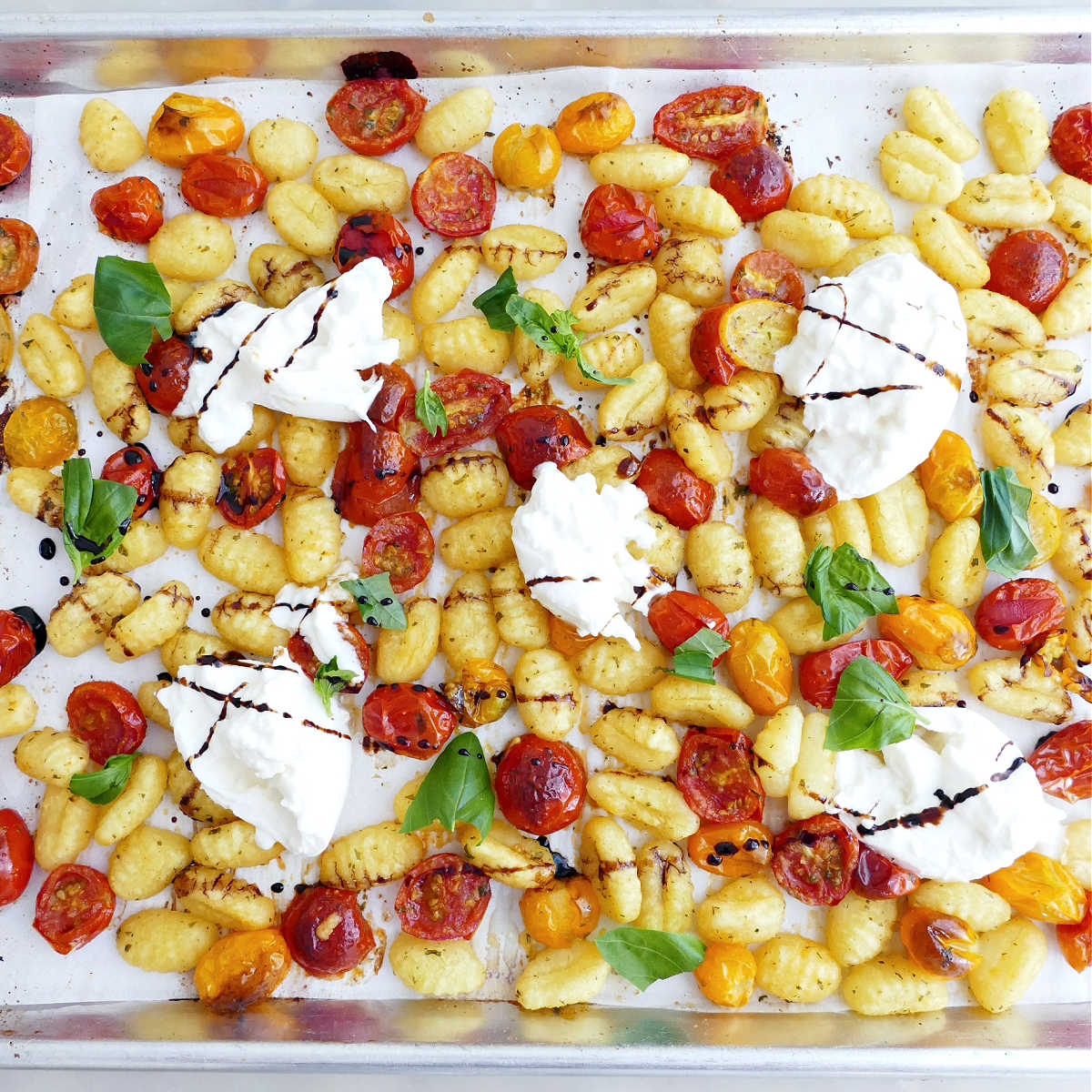Roasted gnocchi and tomatoes with burrata, balsamic glaze, and basil on a sheet pan.
