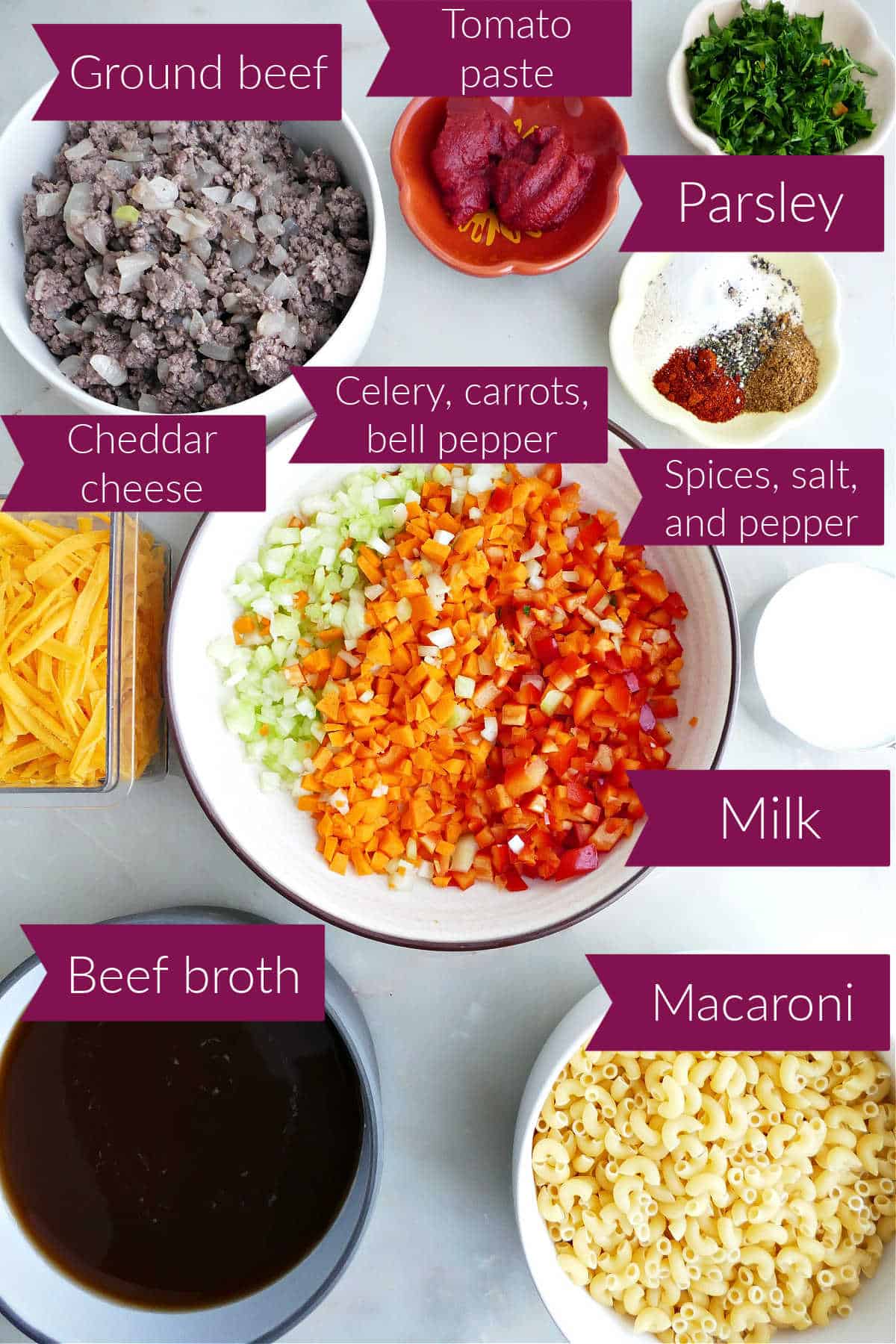 Cheese, beef, tomato paste, parsley, spices, milk, vegetables, macaroni, and broth on a counter.