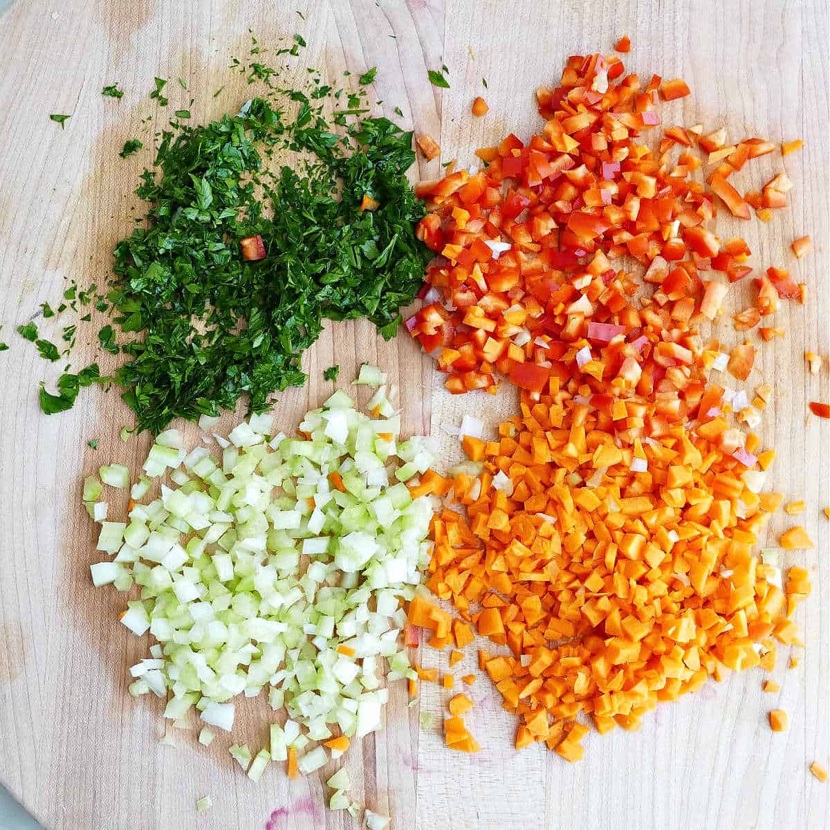 Finely chopped parsley, bell pepper, celery, and carrots on a cutting board.