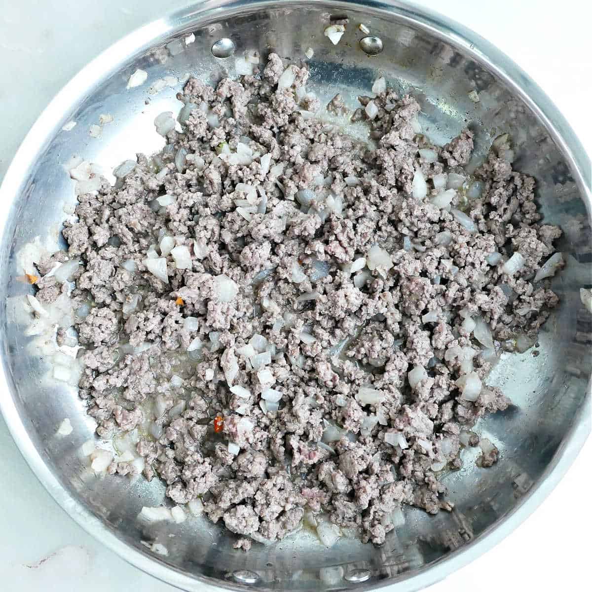 Ground beef and diced onion cooking in olive oil in a skillet.