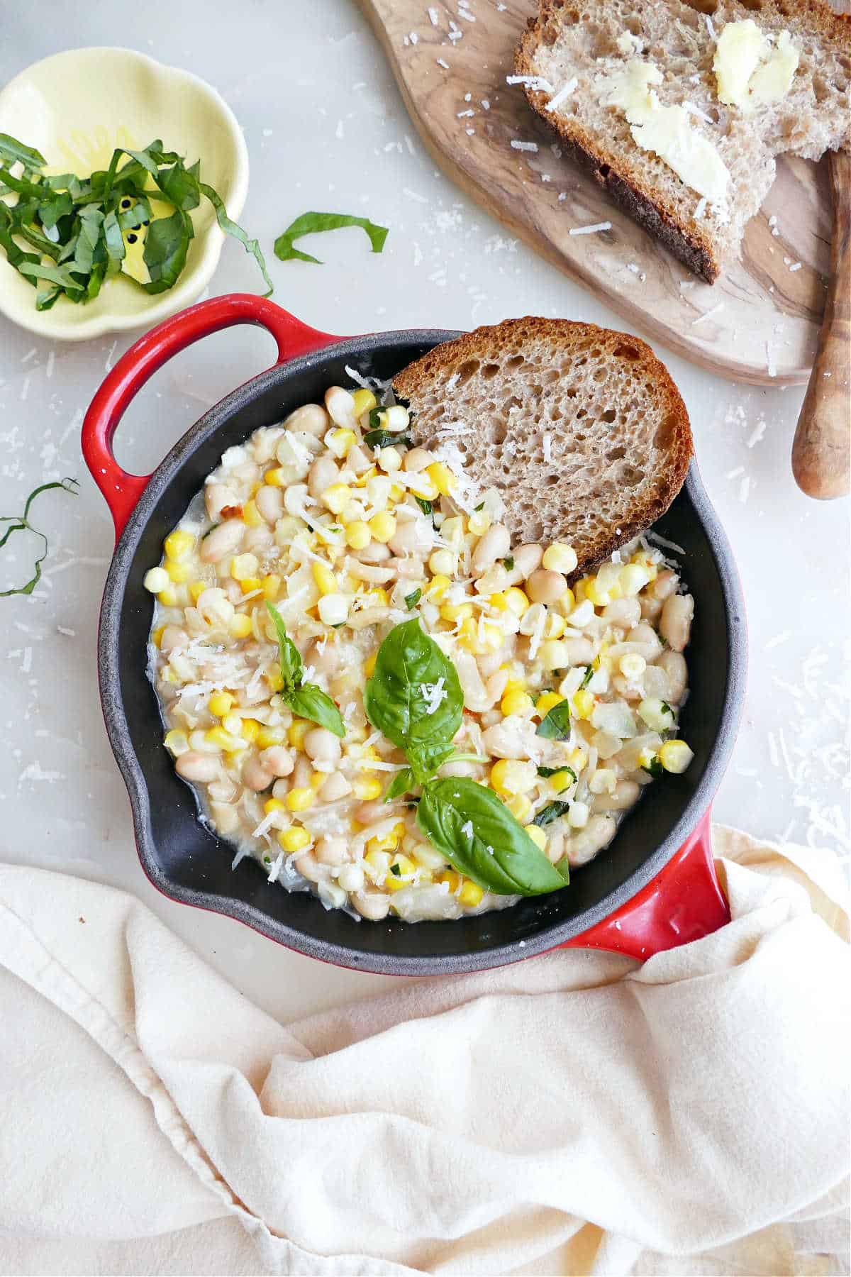 White beans, corn, basil, and bread in a red skillet next to ingredients.
