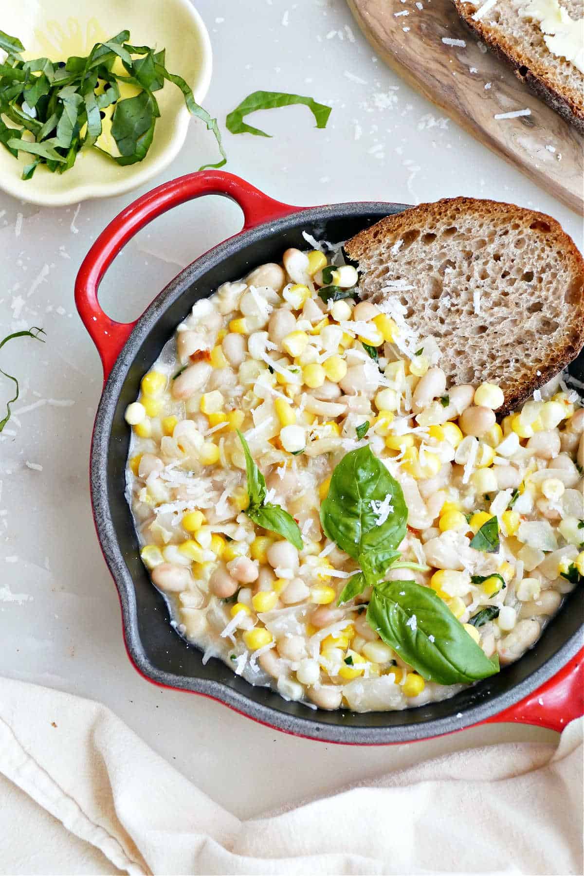 Creamy white bean skillet with basil and bread on a counter.