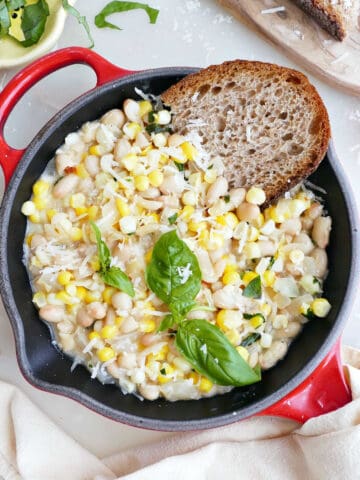 White beans, corn, basil, and bread in a red skillet next to ingredients.