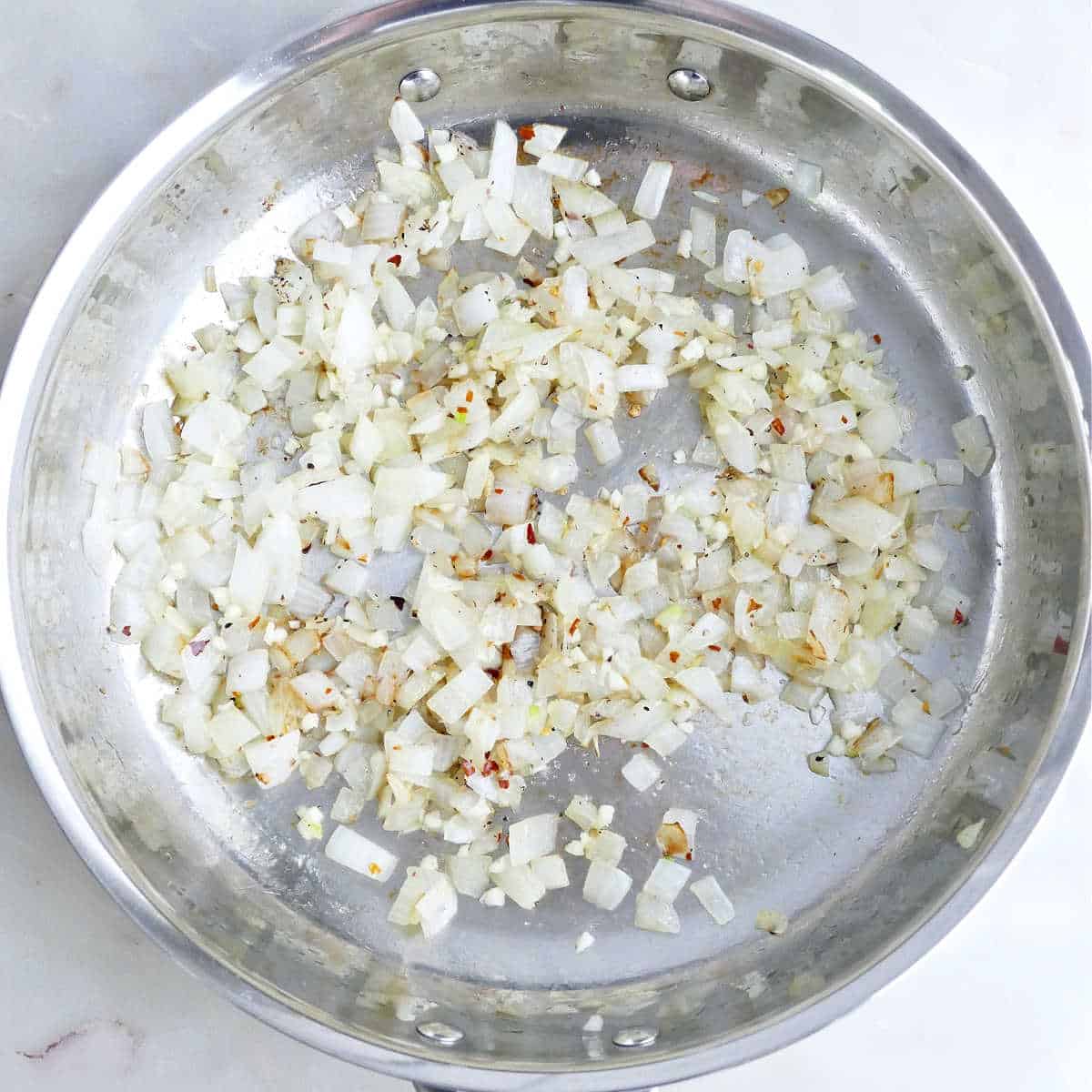 Onions, garlic, and seasonings cooking in olive oil in a skillet.
