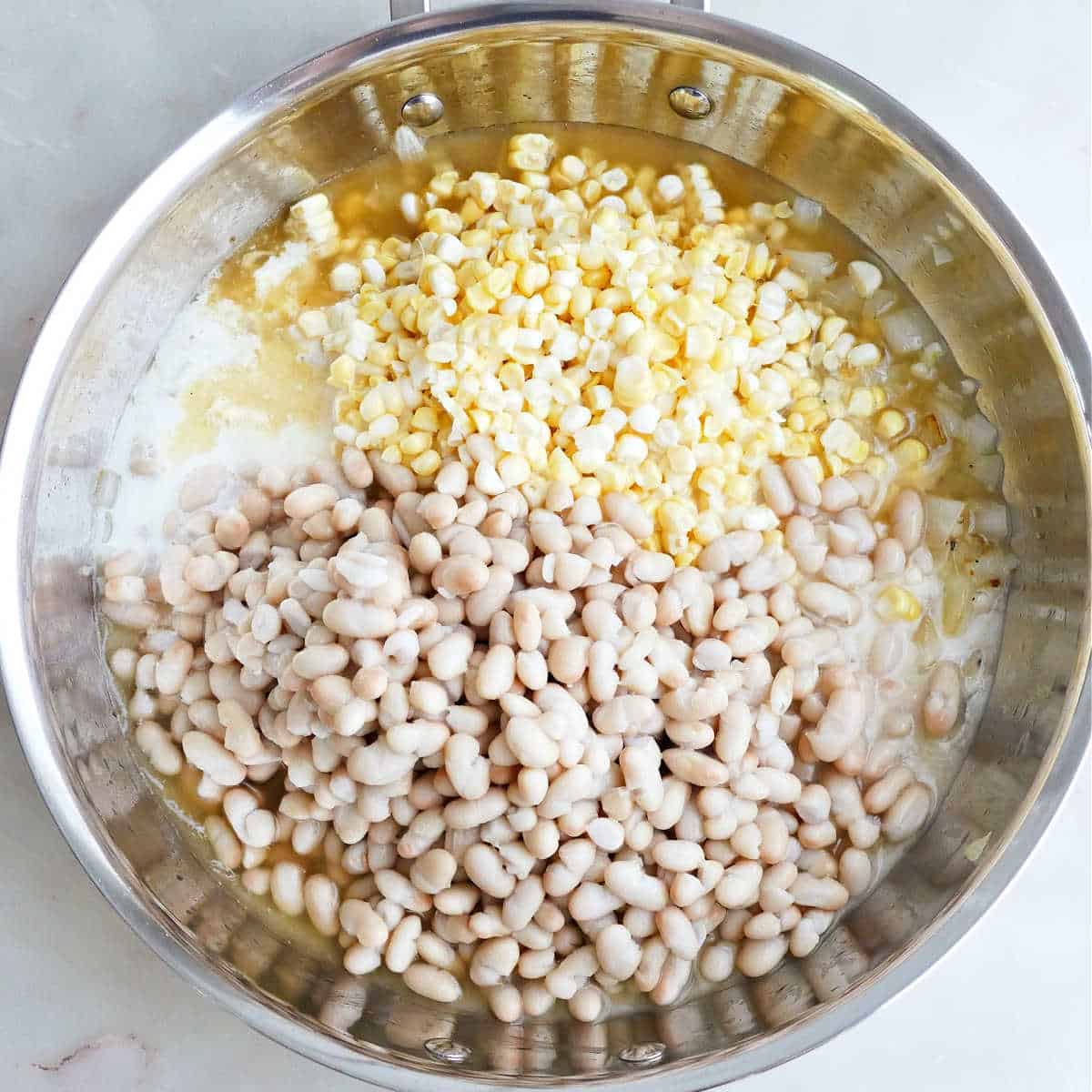 Corn, white beans, milk, broth, and lemon juice added to a skillet.