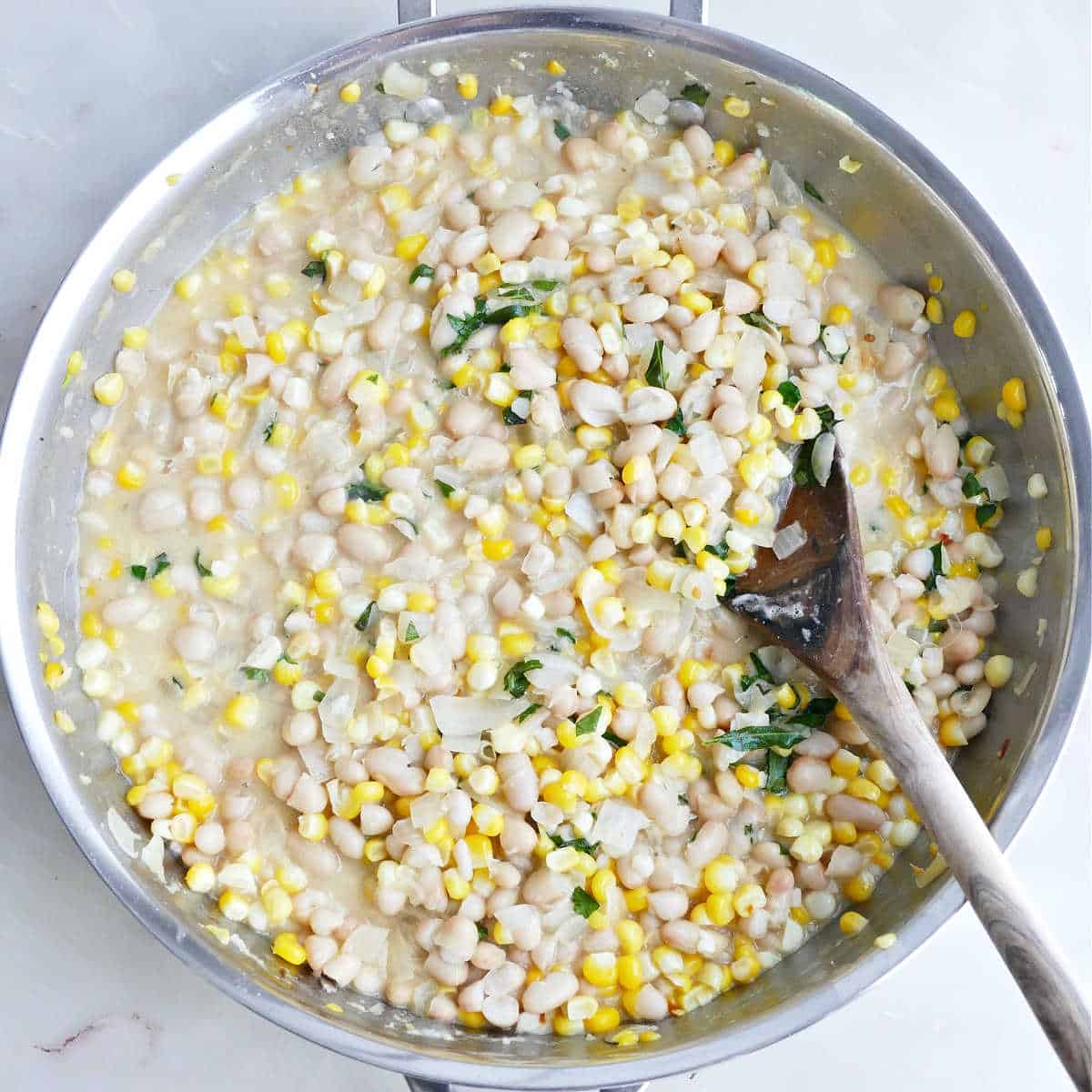 Creamy white bean skillet with corn being stirred with a wooden spoon.