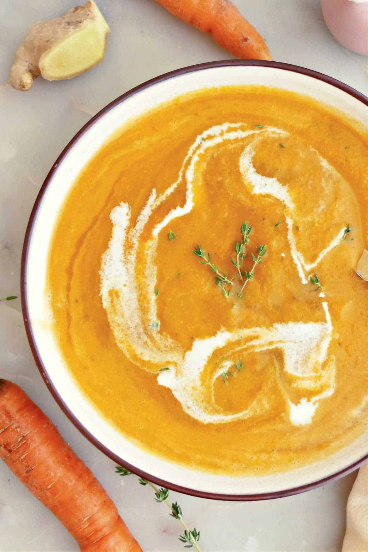 Apple carrot ginger soup with heavy cream and thyme in a bowl.