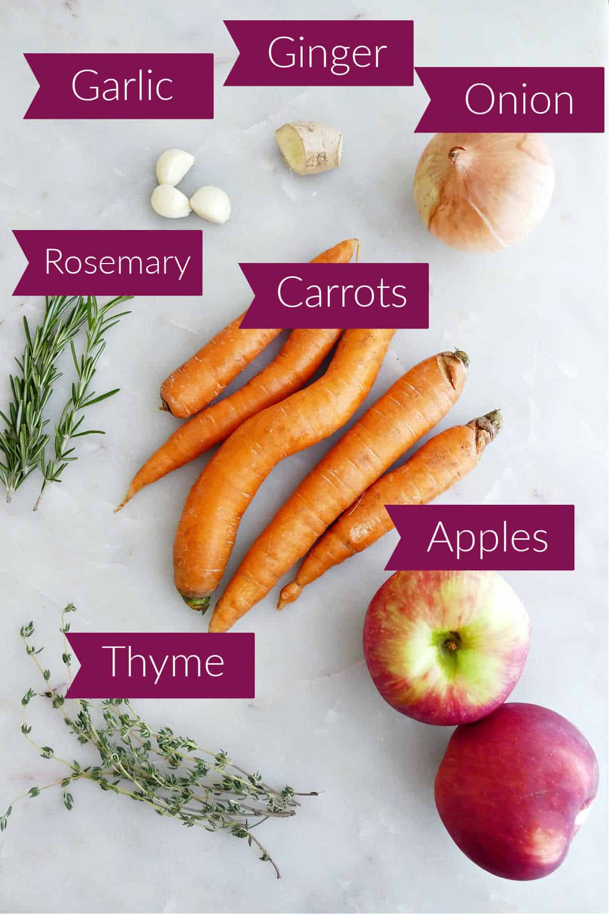 Garlic, ginger, onion, carrots, apples, thyme, and rosemary on a counter with labels.