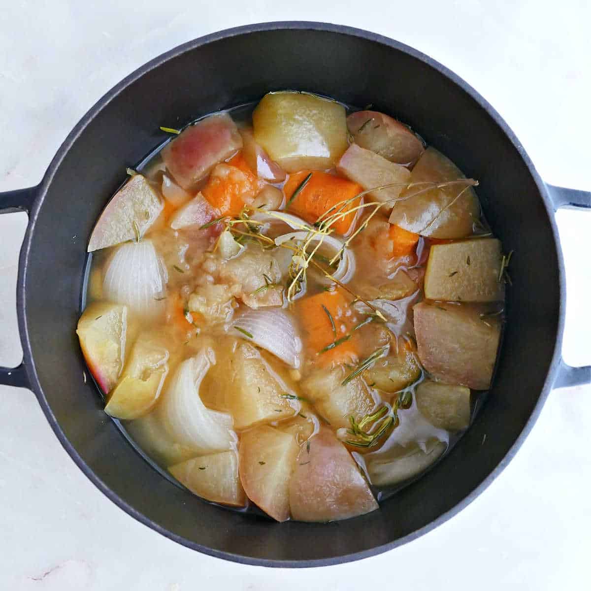 Ingredients for carrot soup with apples, onion, and ginger in a pot after simmering.