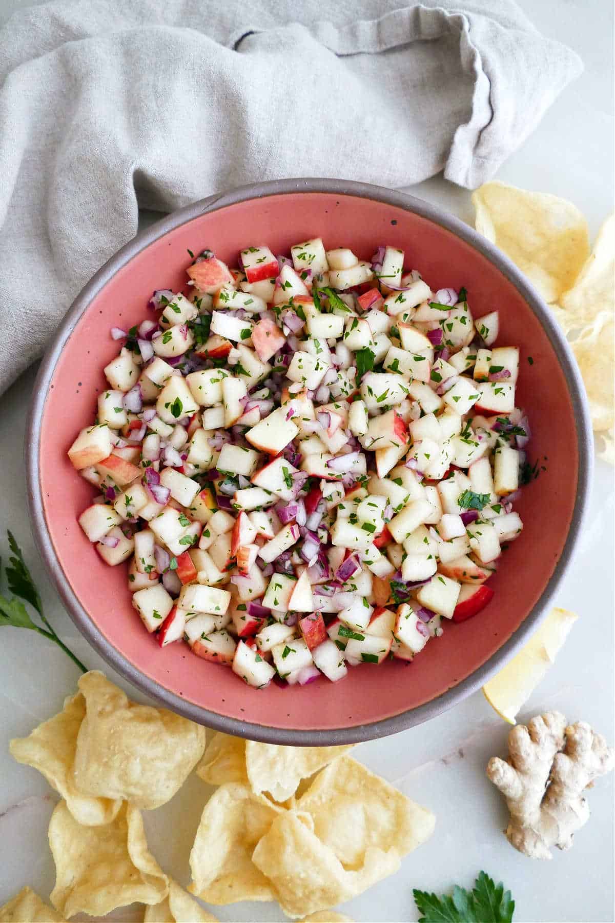 Apple salsa in a serving bowl surrounded by chips, a napkin, and ginger root.