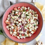 Apple salsa in a serving bowl surrounded by chips, a napkin, and ginger root.
