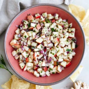 Apple salsa in a serving bowl surrounded by chips, a napkin, and ginger root.