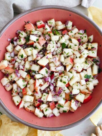 Apple salsa in a serving bowl surrounded by chips, a napkin, and ginger root.