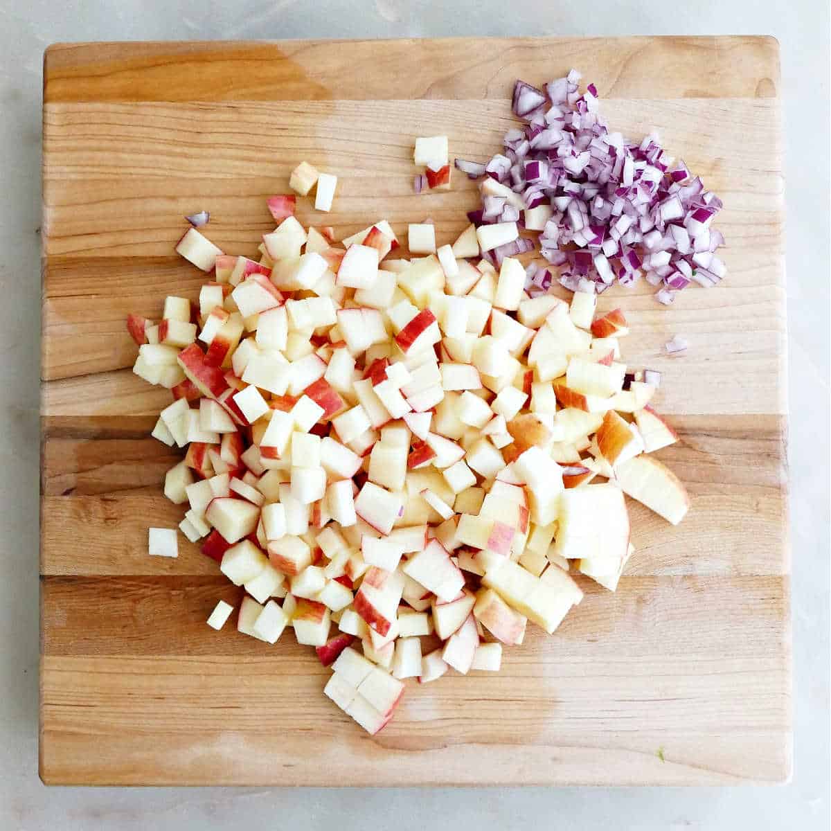 Cubed apples and diced red onion on a wooden cutting board.