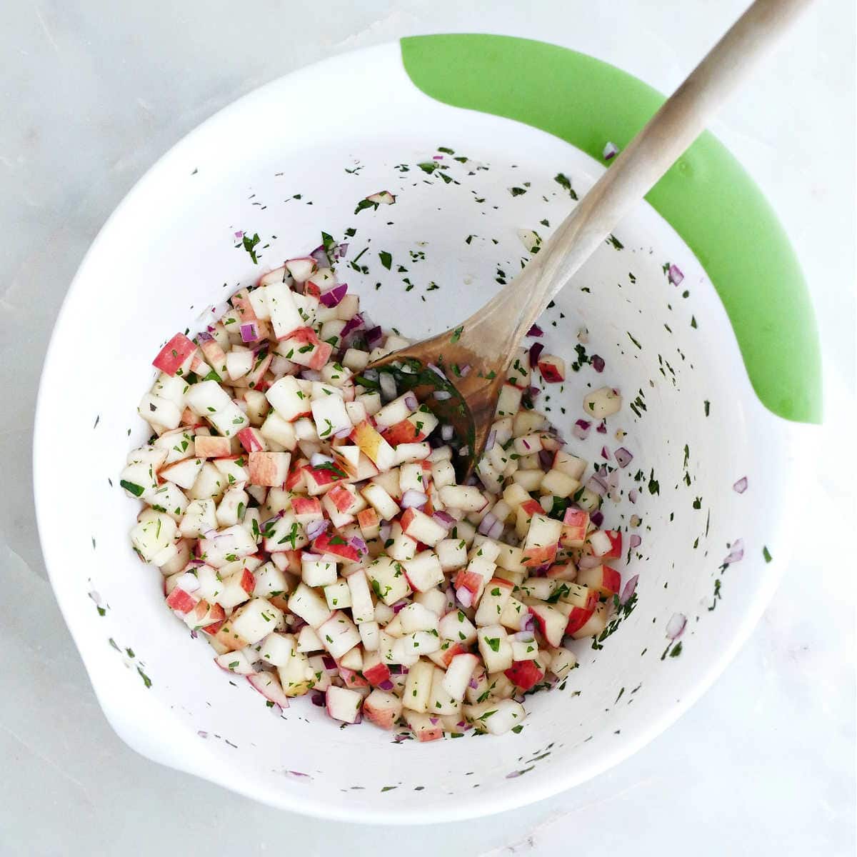 Ingredients for sweet salsa with apples stirred together in a bowl with a spoon.