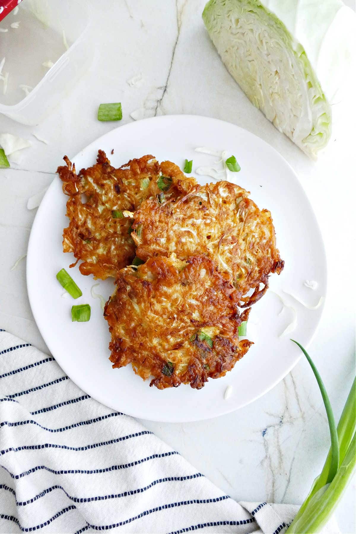 Three cabbage fritters on a plate surrounded by a napkin and ingredients.