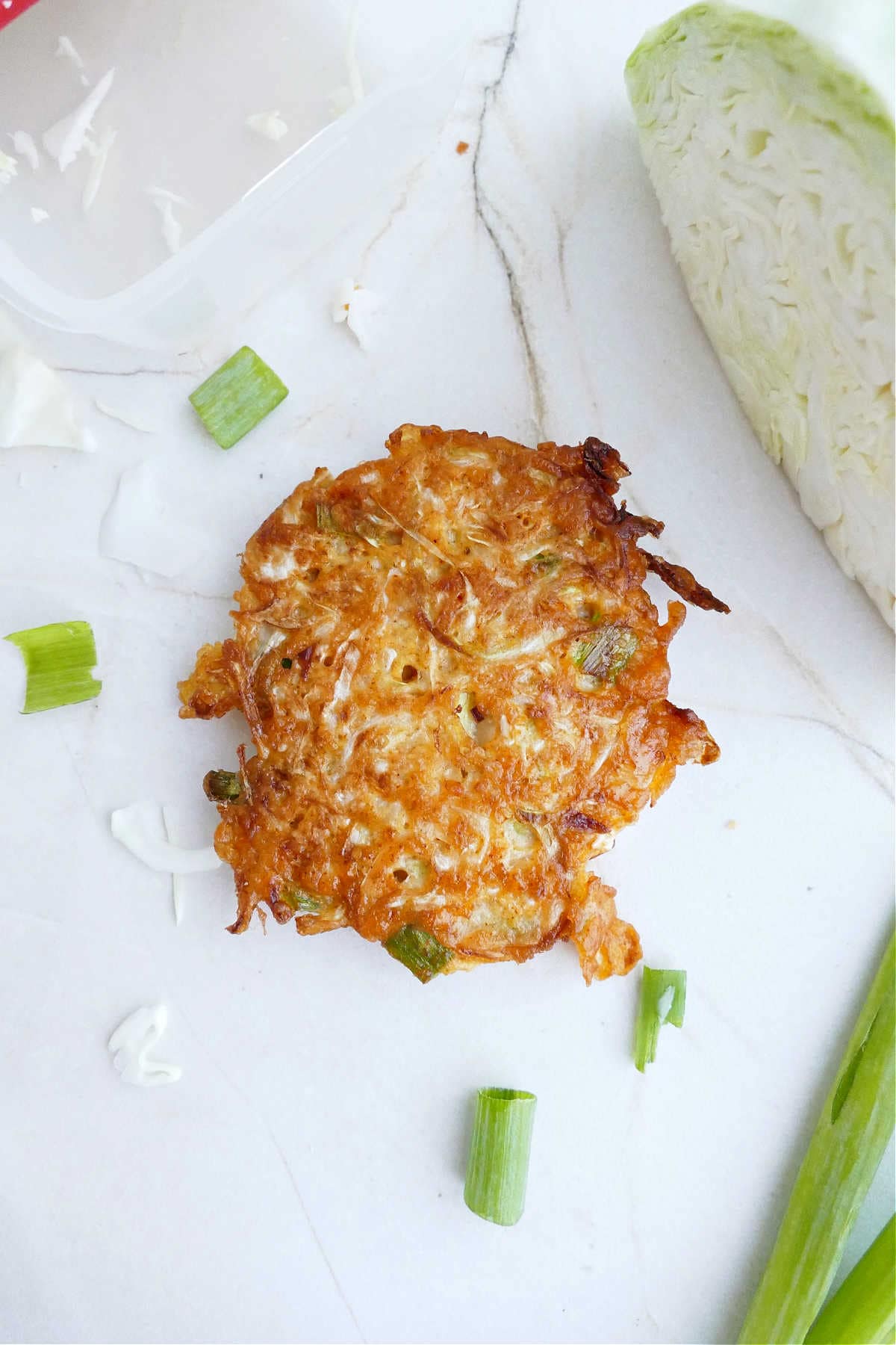 Crispy cabbage fritter on a counter sprinkled with scallions.