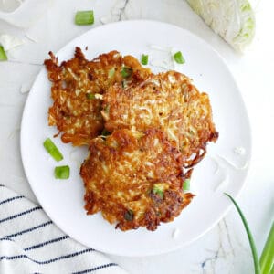 Three cabbage fritters on a plate surrounded by a napkin and ingredients.