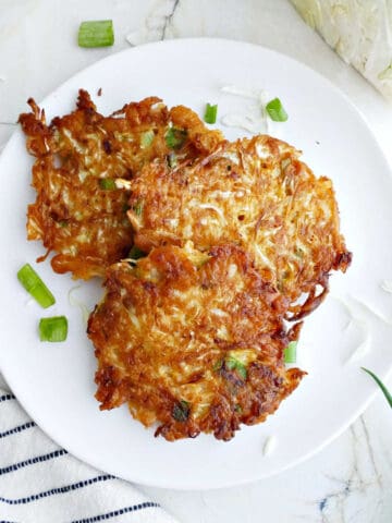 Three cabbage fritters on a plate surrounded by a napkin and ingredients.