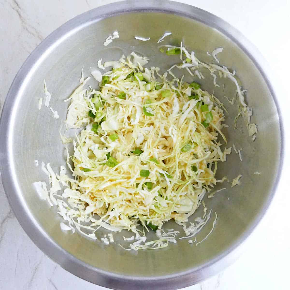 Shredded cabbage and scallions coated in eggs in a bowl.