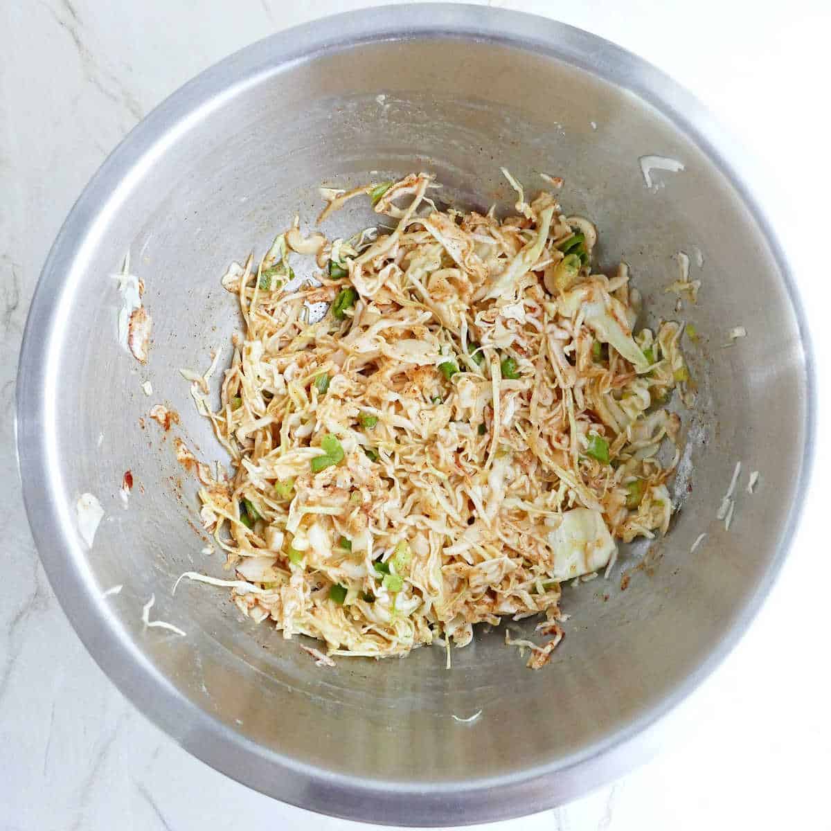 Shredded cabbage, eggs, flour, and spices in a bowl.