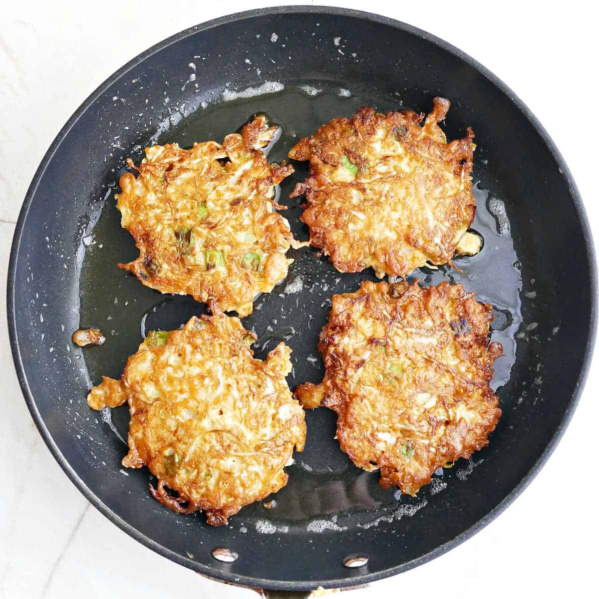 Four cabbage fritters after cooking in a skillet.