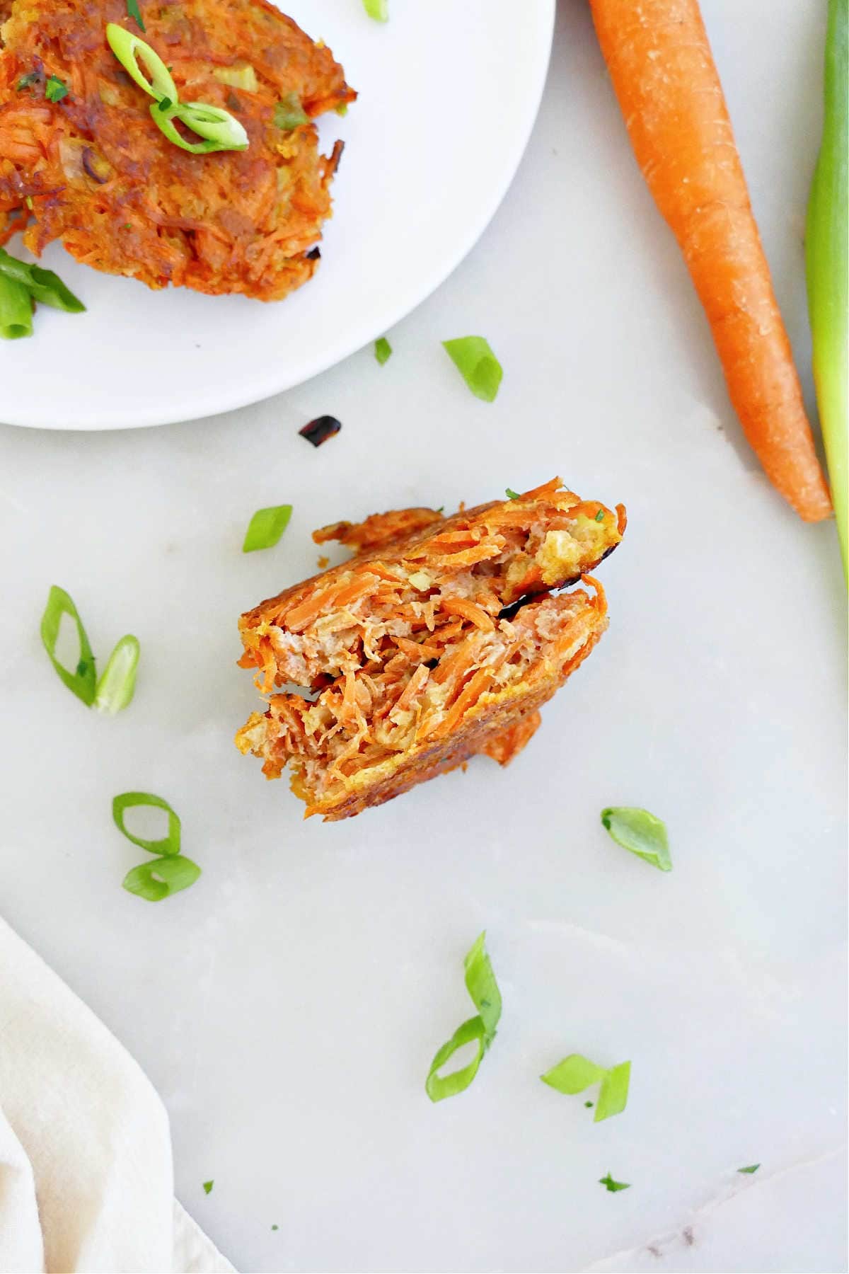 A carrot patty sliced in half on a counter next to ingredients and a serving plate.
