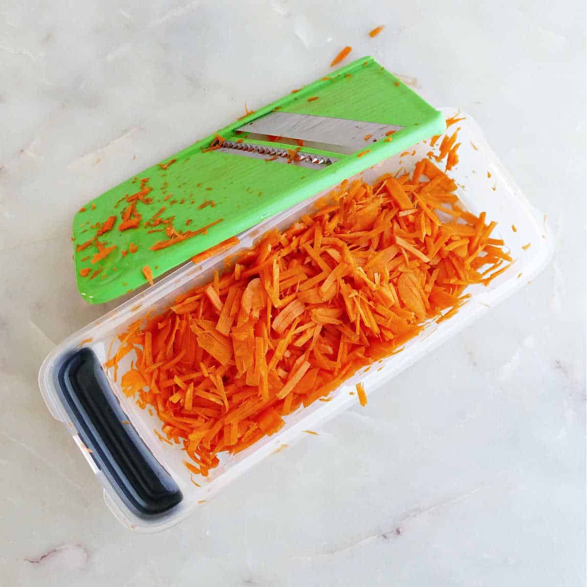Grated carrots in a container next to grating blade.