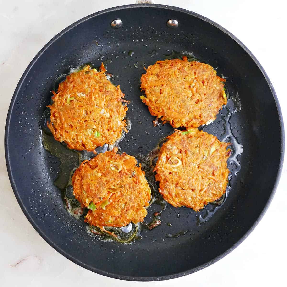 Four carrot patties after being cooked on both sides in a skillet.