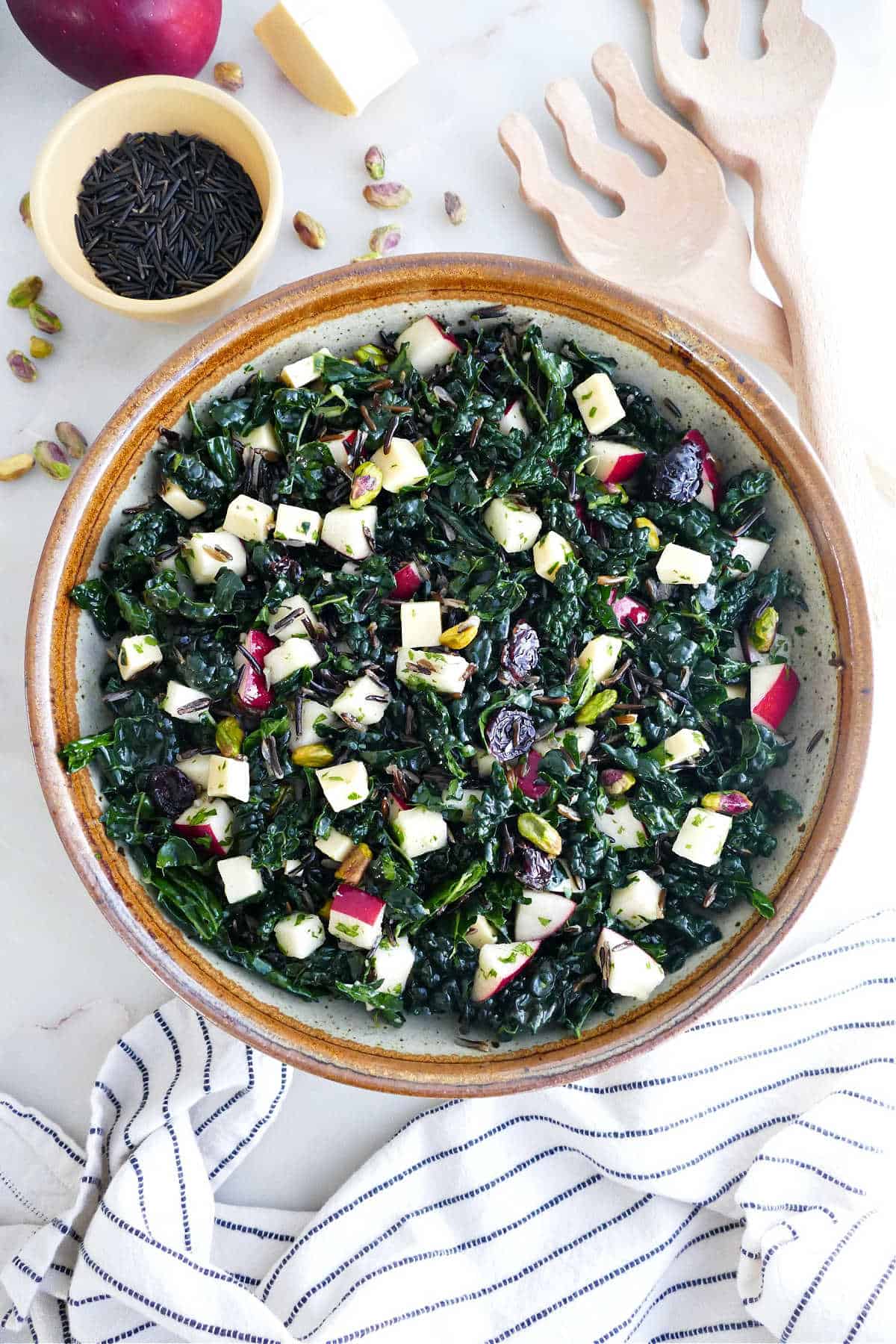 Kale wild rice salad in a serving bowl next to ingredients, napkins, and serving utensils.