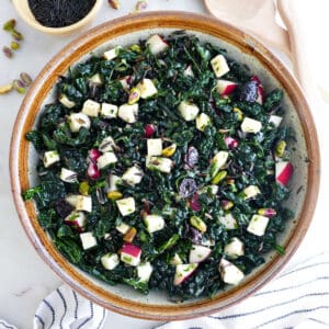 Kale wild rice salad in a serving bowl next to ingredients, napkins, and serving utensils.