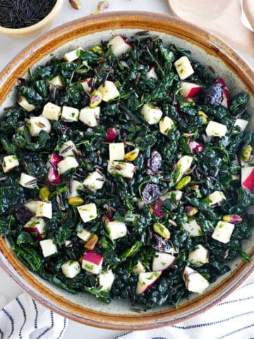 Kale wild rice salad in a serving bowl next to ingredients, napkins, and serving utensils.