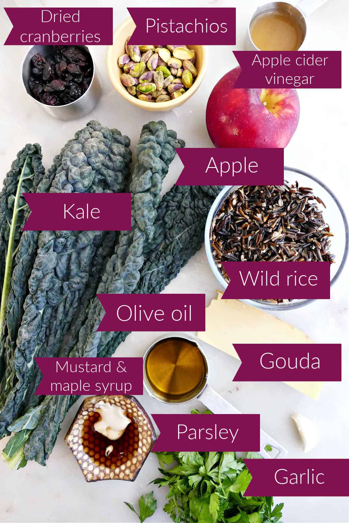 Dried cranberries, pistachios, vinegar, apple, rice, cheese, garlic, parsley, oil, mustard, syrup, and kale with labels.