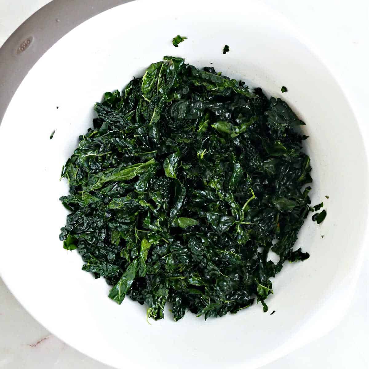 Shredded kale massaged with olive oil in a mixing bowl.