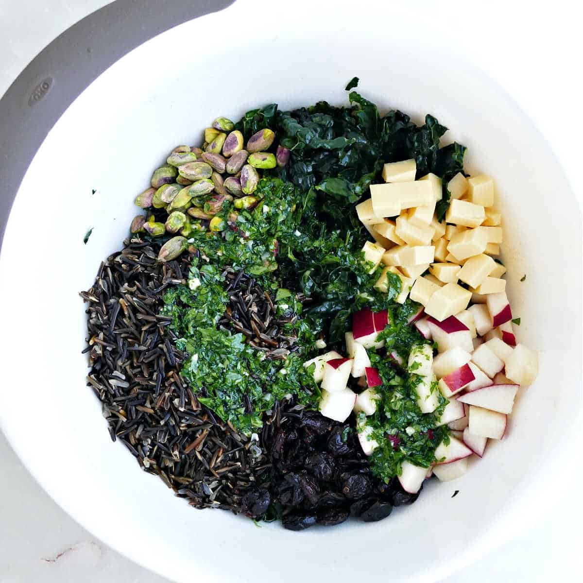 Ingredients for kale salad drizzled with parsley apple cider vinaigrette in a mixing bowl.