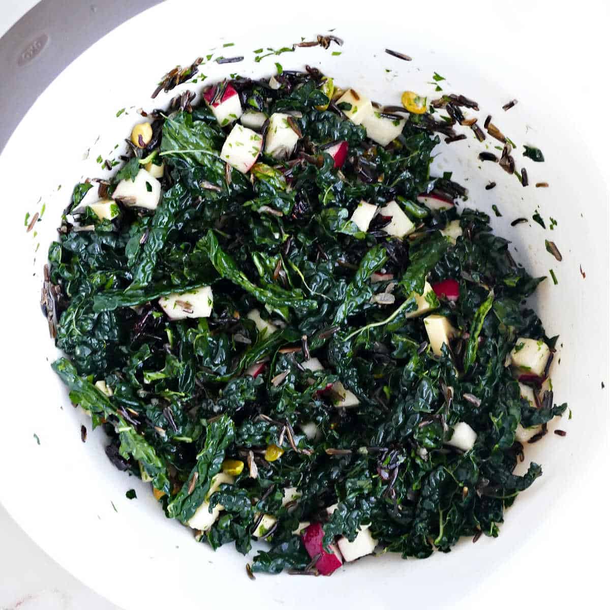 Kale wild rice salad tossed in dressing in a mixing bowl.