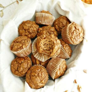 Pumpkin banana muffins in a basket lined with a napkin surrounded by ingredients.