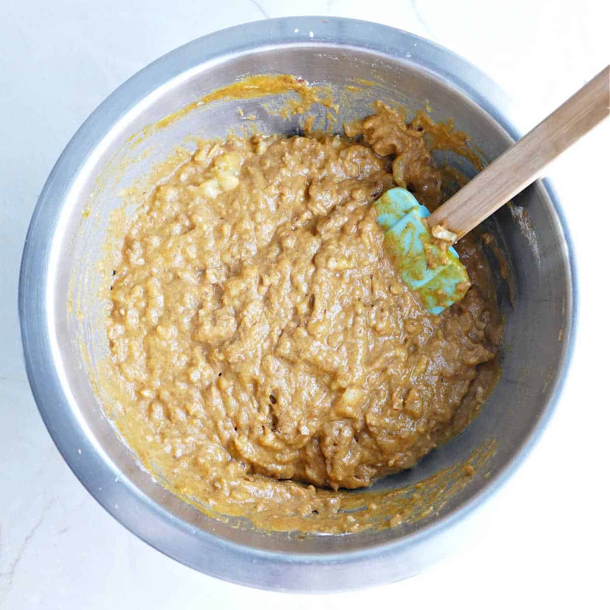 Dry and wet ingredients for muffins stirred together in a bowl with a spatula.