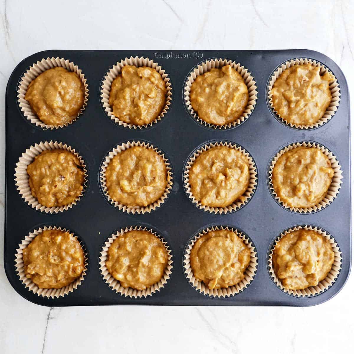 Pumpkin banana muffins in a muffin tin with liners before baking in the oven.