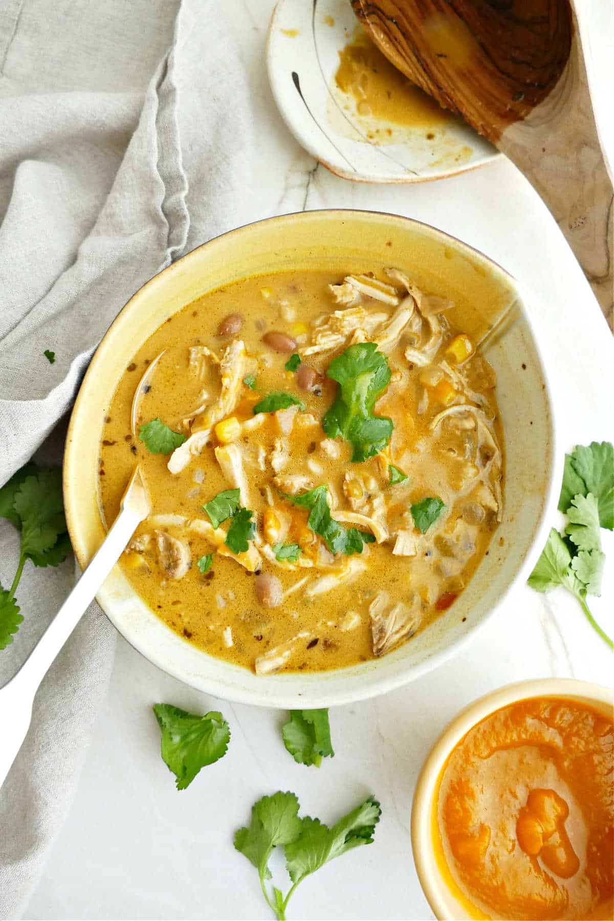 Pumpkin chicken soup with cilantro in a bowl with spoon surrounded by ingredients.