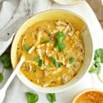 Pumpkin chicken soup with cilantro in a bowl with spoon surrounded by ingredients.