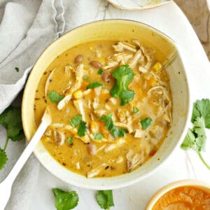 Pumpkin chicken soup with cilantro in a bowl with spoon surrounded by ingredients.
