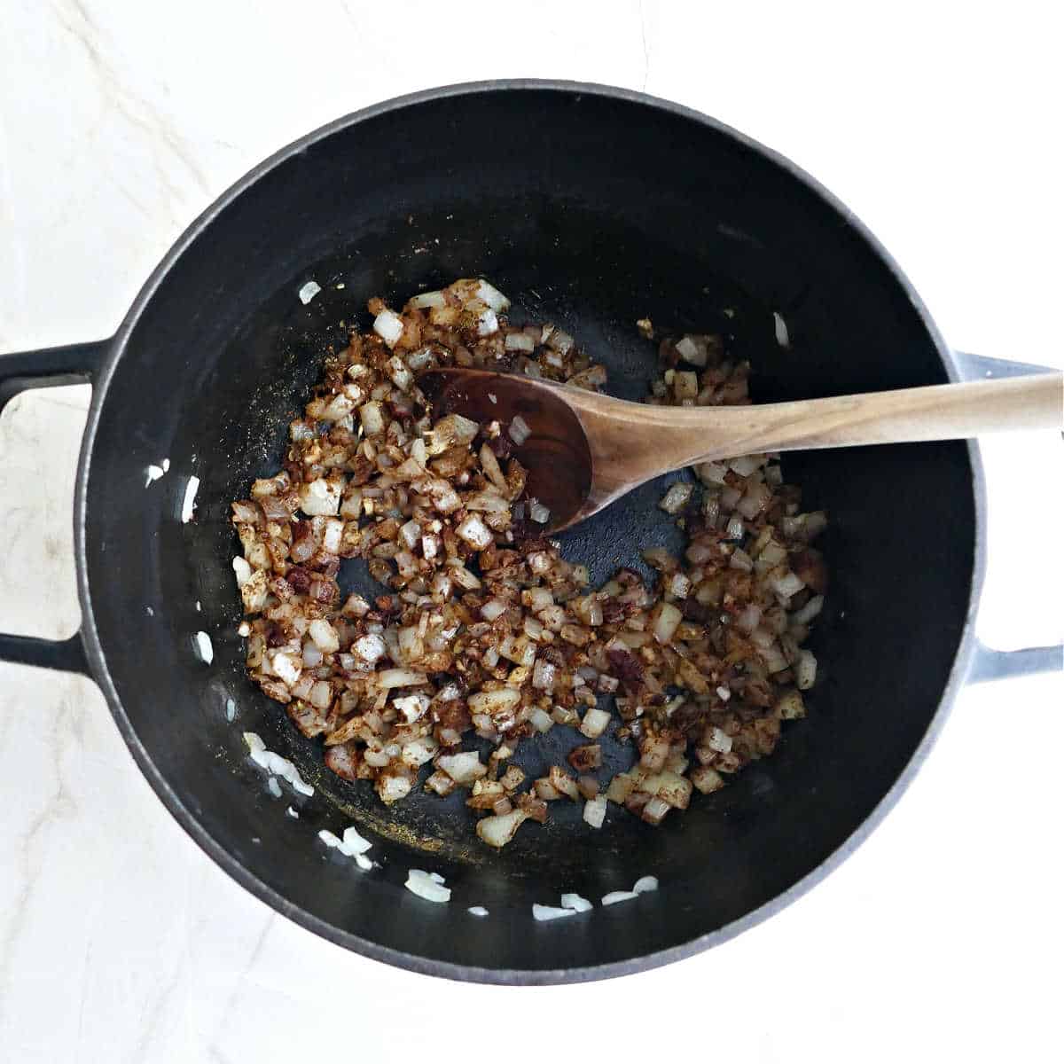 Onions and garlic cooking with warm spices in a pot with a spoon.