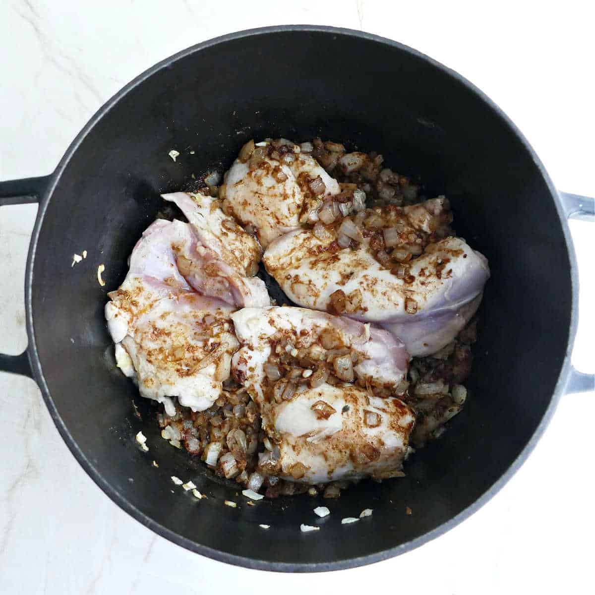 Chicken thighs being seared in a soup pot with spices.