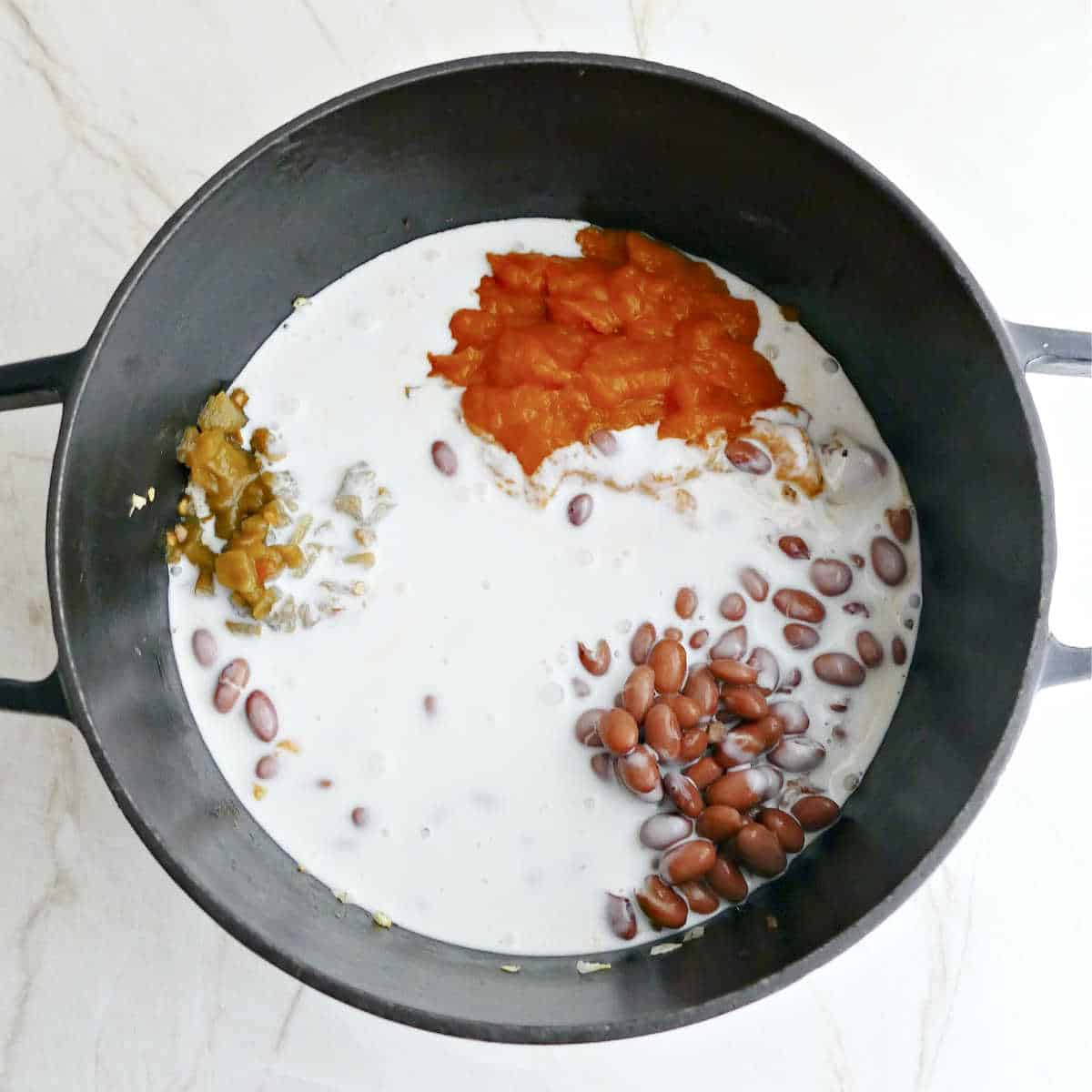 Pumpkin, coconut milk, beans, and green chiles being added to a soup pot.