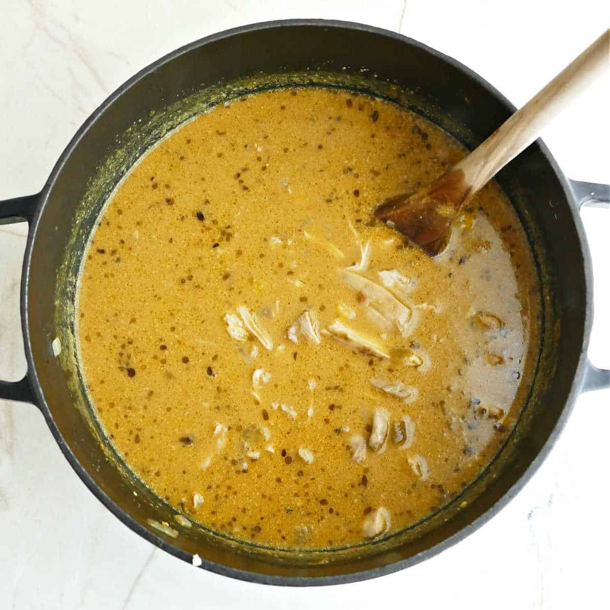 Pumpkin soup with shredded chicken and corn added to it in a pot with a spoon.