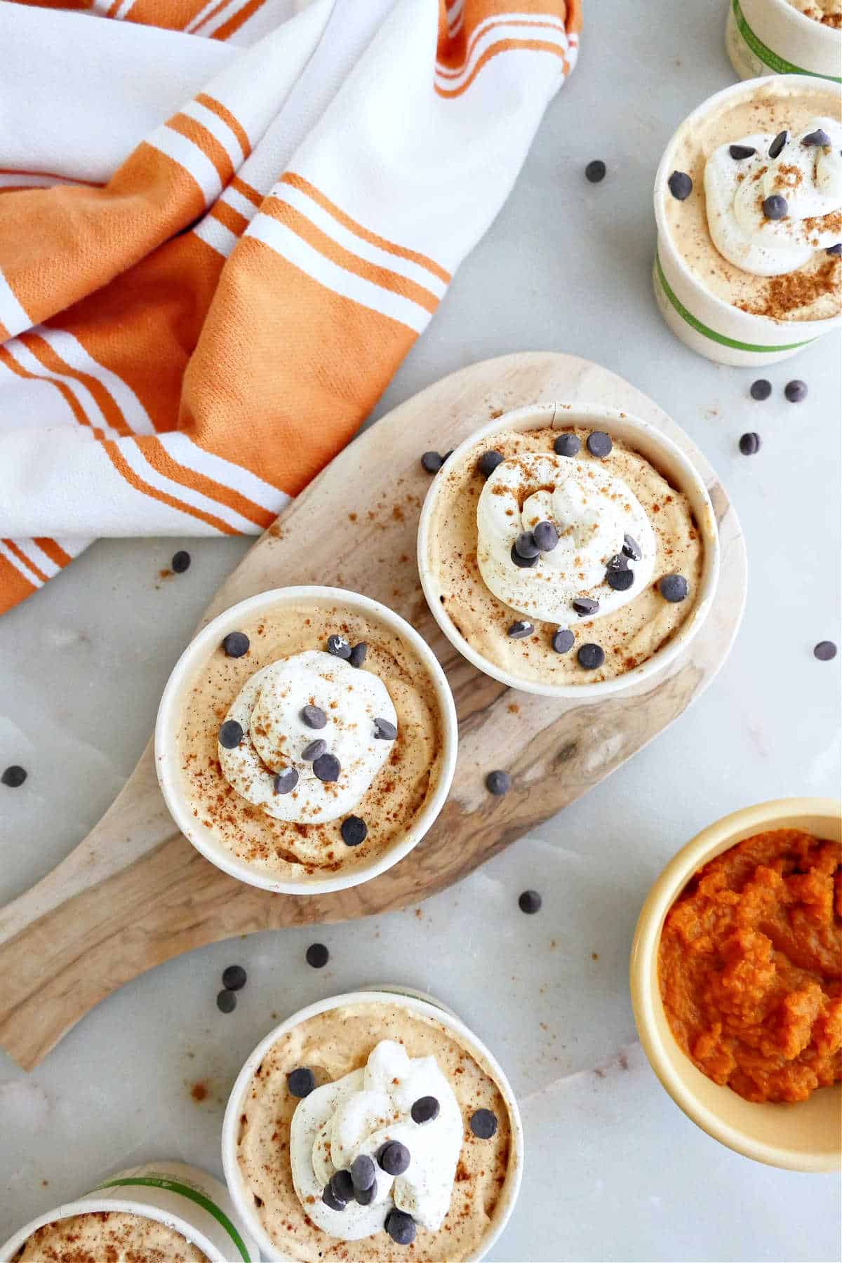 Pumpkin mousse with whipped cream and chocolate chips in cups on a counter.