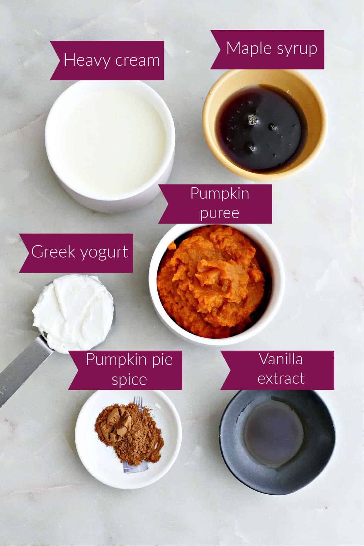 Heavy cream, maple syrup, yogurt, pumpkin puree, pumpkin spice, and vanilla with labels on a counter.