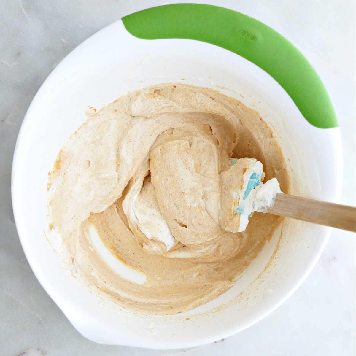 Whipped cream being folded into pumpkin mousse with a spatula in a bowl.