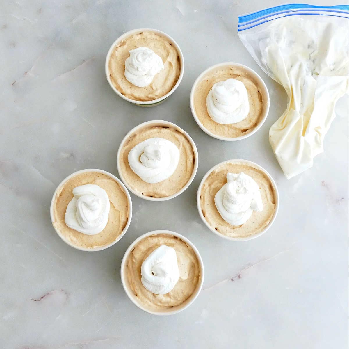 Pumpkin mousse spooned into cups and topped with whipped cream from a piping bag.